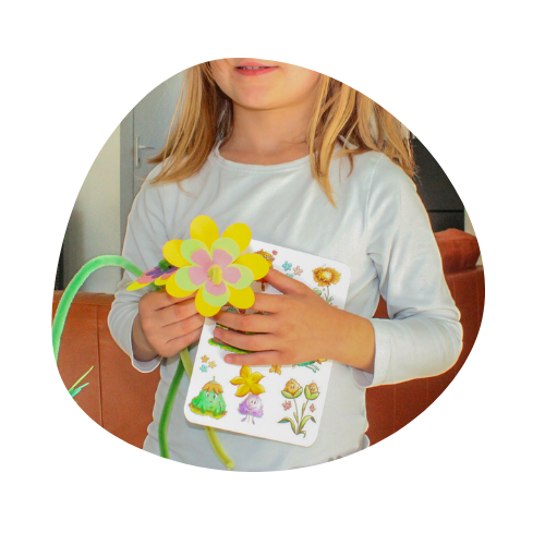 Enfant qui tient une fleur réalisé avec le kit papeterie pour jouer fleuriste et la planche de stickers présente dans le kit.
